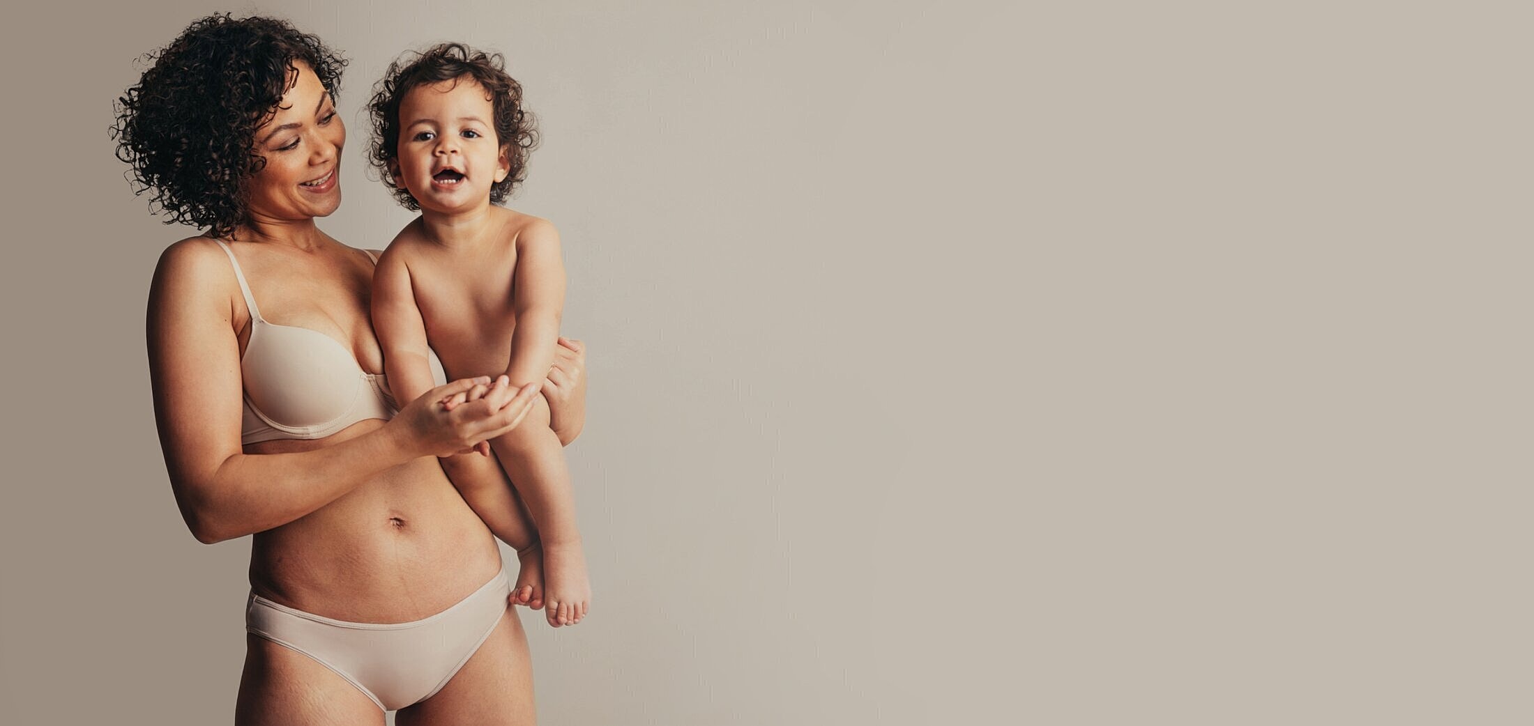 Mother holding smiling child against neutral background.