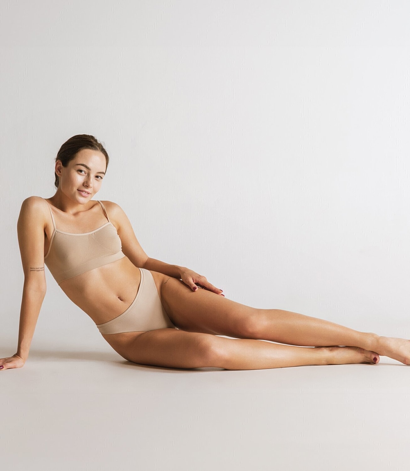 Model in neutral lingerie posing on white background.