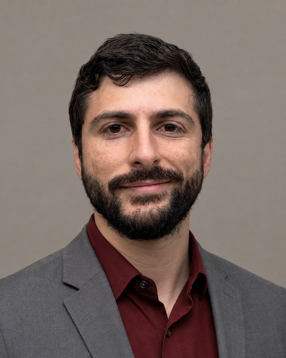 Man with beard in suit against neutral background.