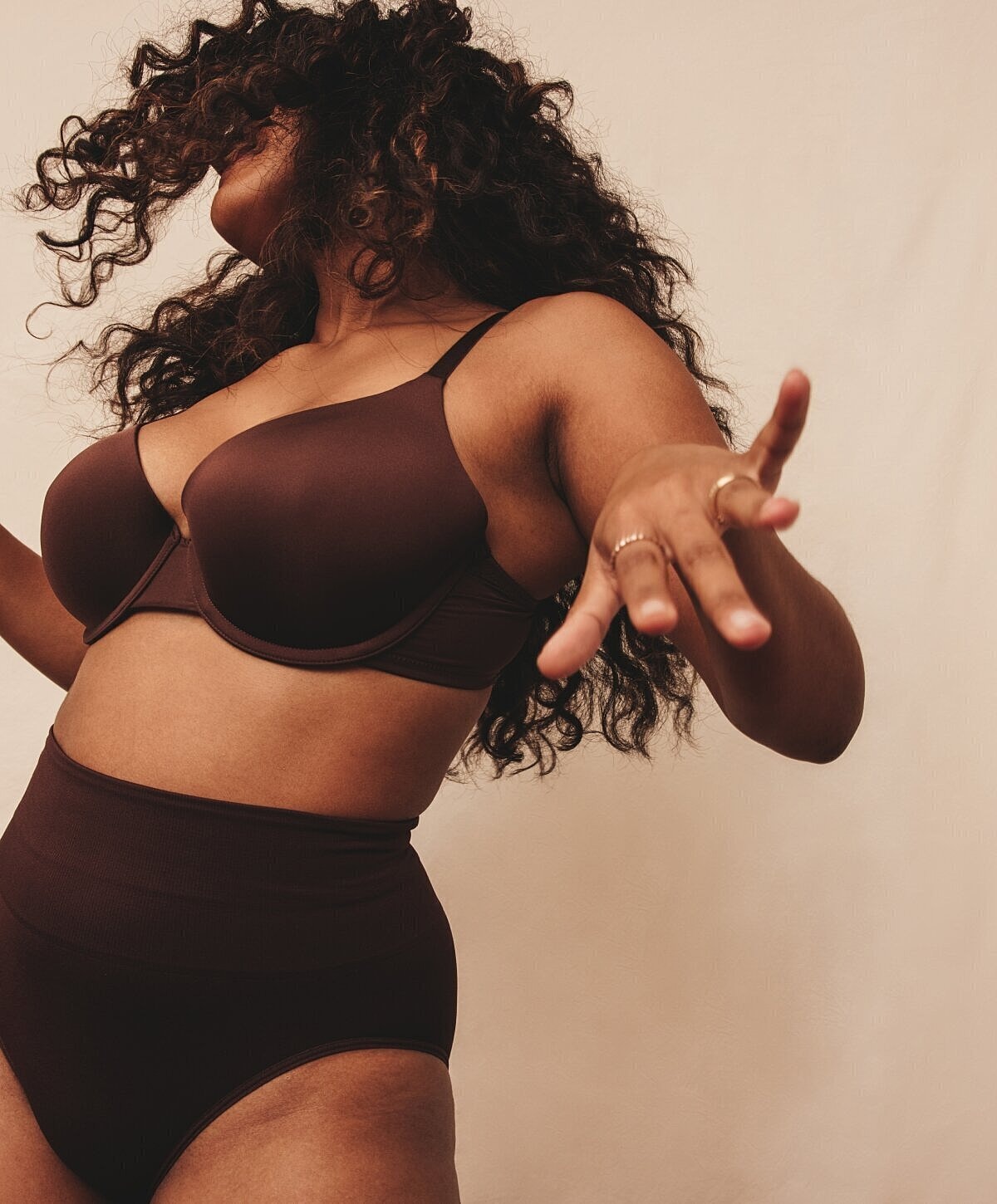 Curly-haired woman in brown lingerie posing playfully.
