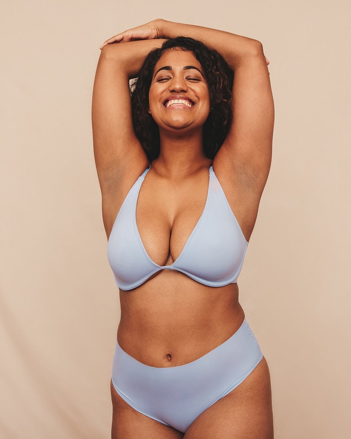 breast augmentation patient model in light blue bra and panties smiling with her arms above her head
