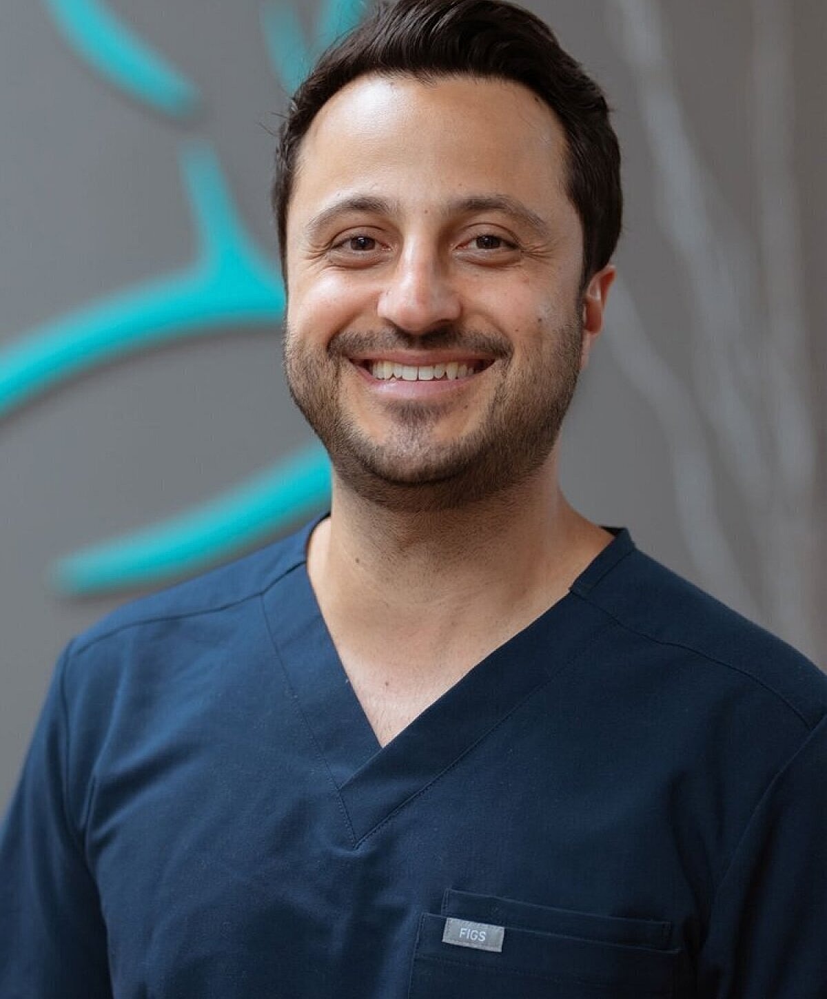 Smiling man in scrubs against a gray background