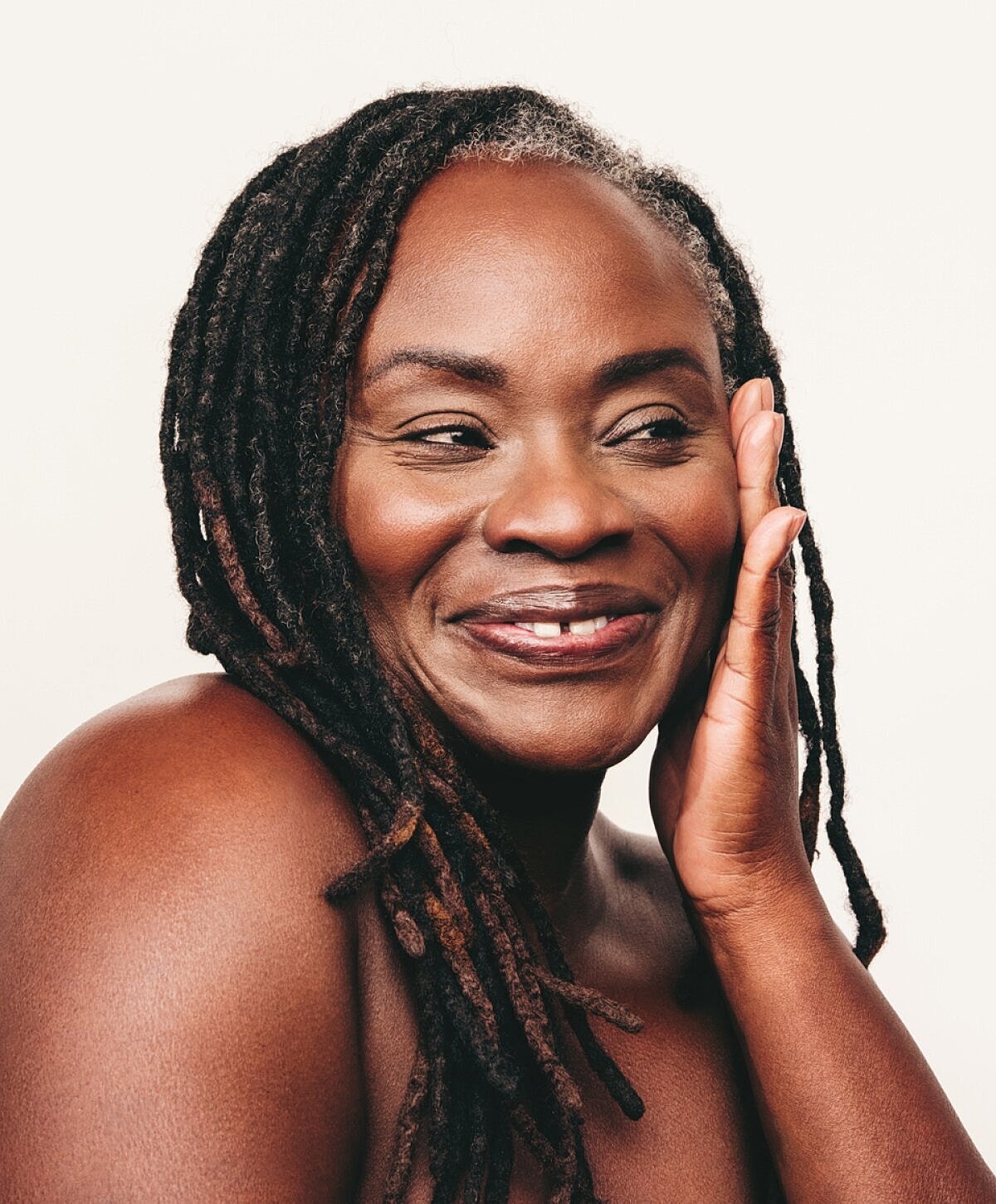 Smiling woman with dreadlocks against neutral background.