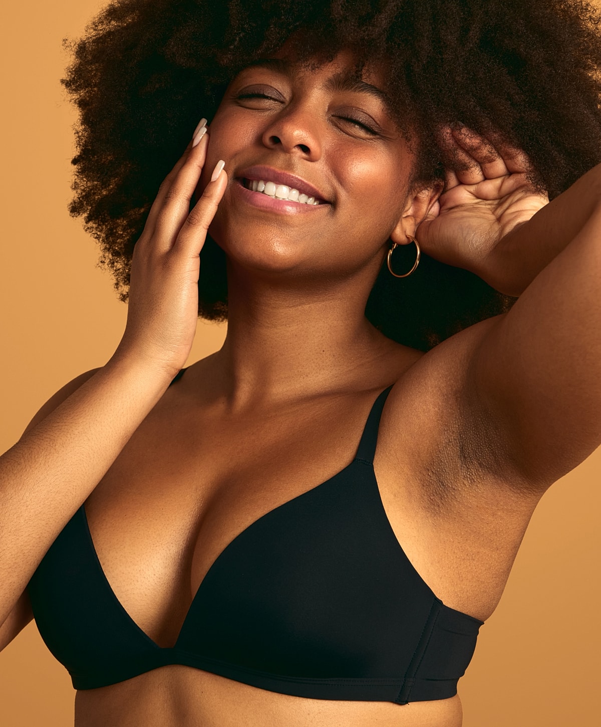 Smiling woman in black bra against orange background.