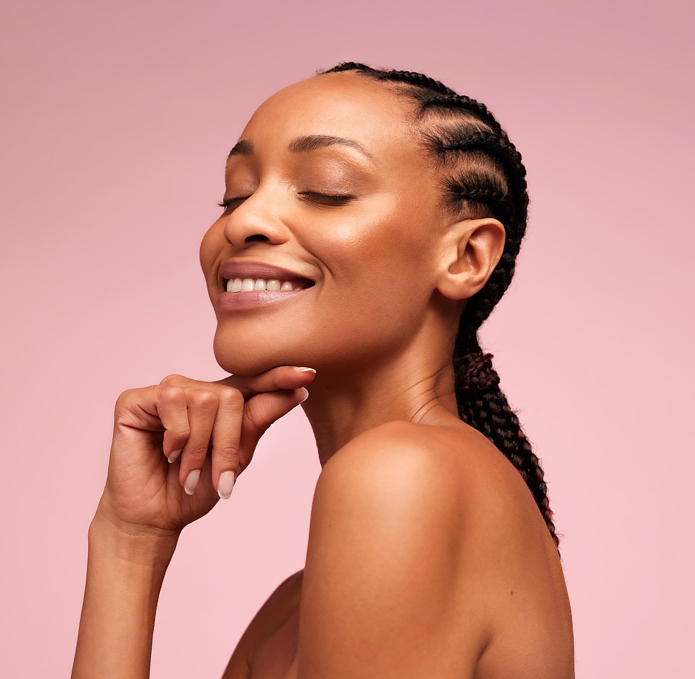 Smiling woman with braided hair against pink background.