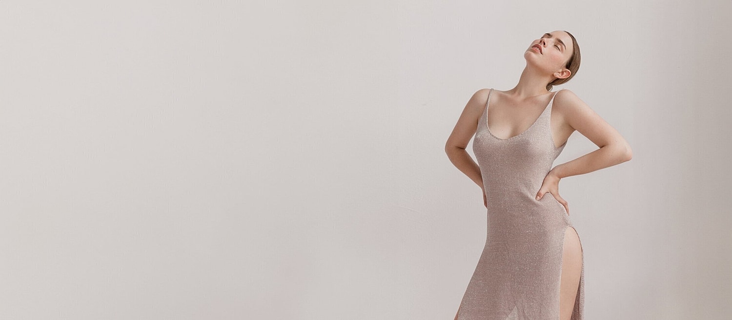 Model in elegant shimmering dress against neutral background.