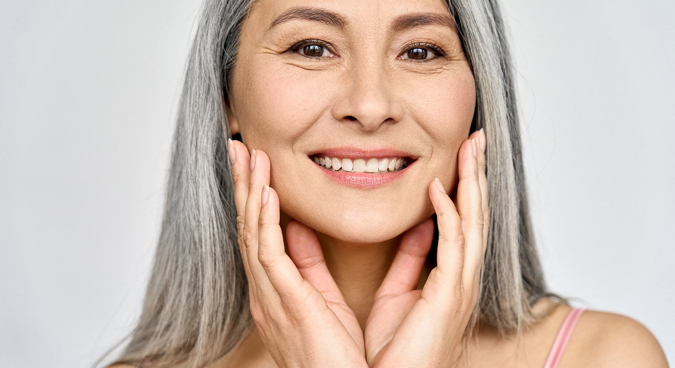 Smiling woman with gray hair touching her face.