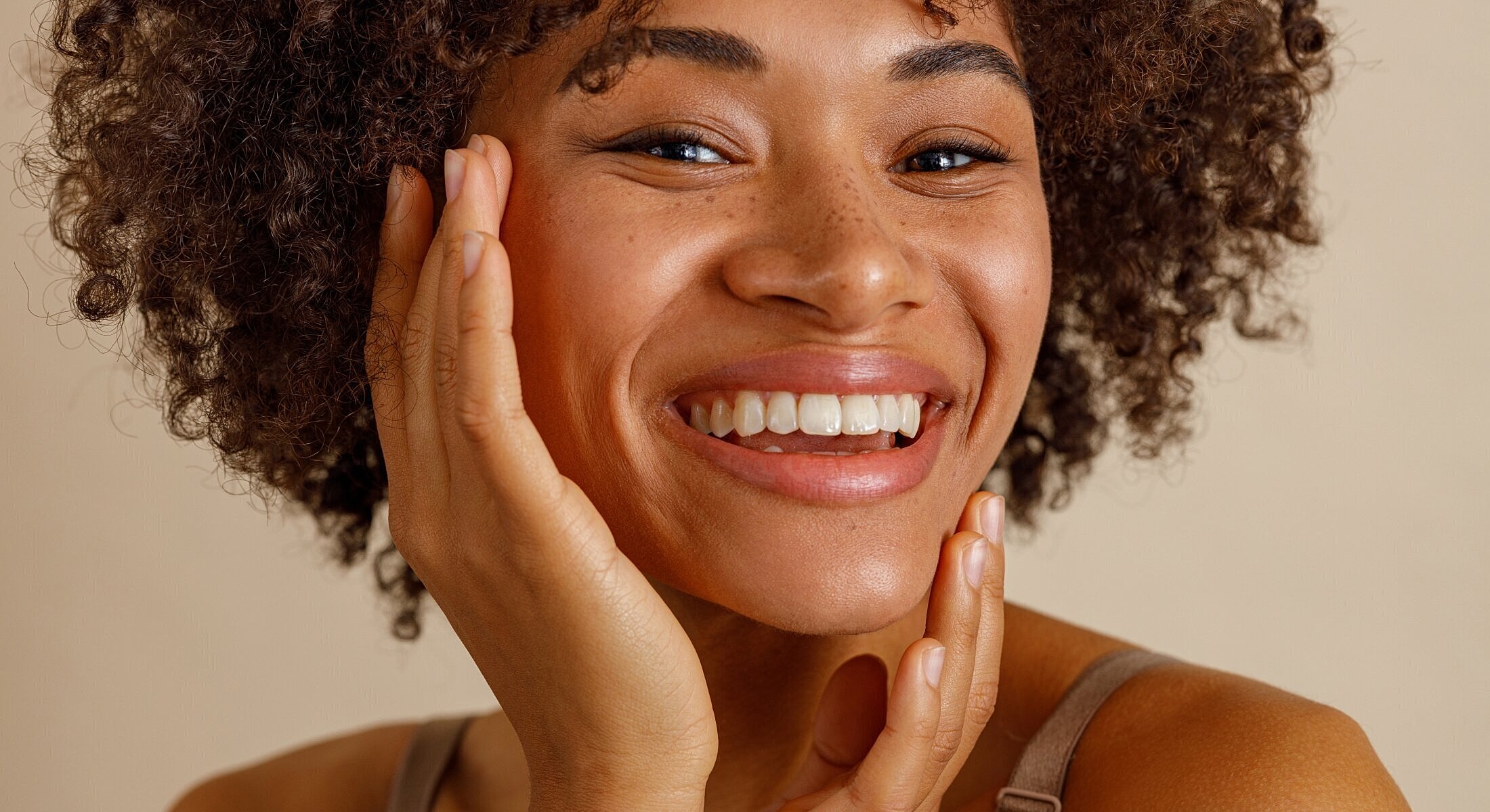 Smiling woman with curly hair and glowing skin.