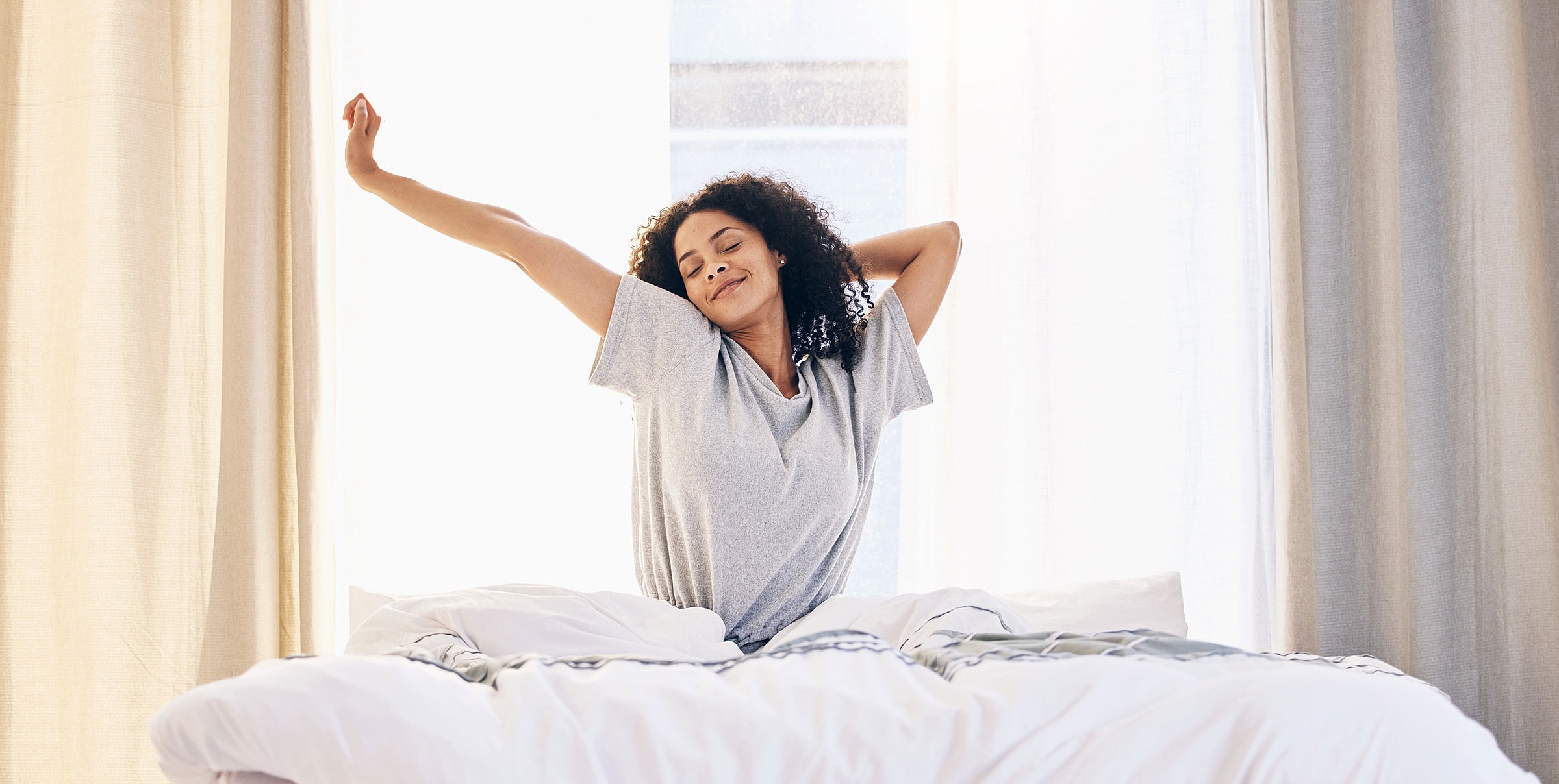 Woman stretching in bed, morning light shining.