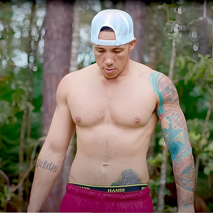 Shirtless man with tattoos outdoors, looking down.