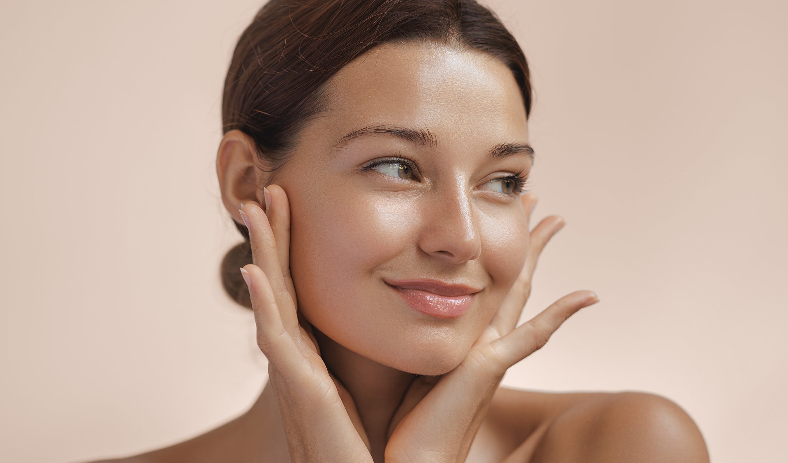 Smiling woman with glowing skin and hands on face.